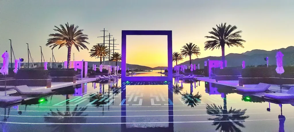 Seaside lounge with palm trees and a lit frame installation at sunset, Montenegro