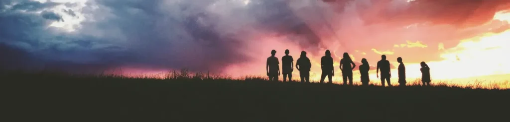 Silhouettes of a group of people on a hilltop under a dramatic sunset sky