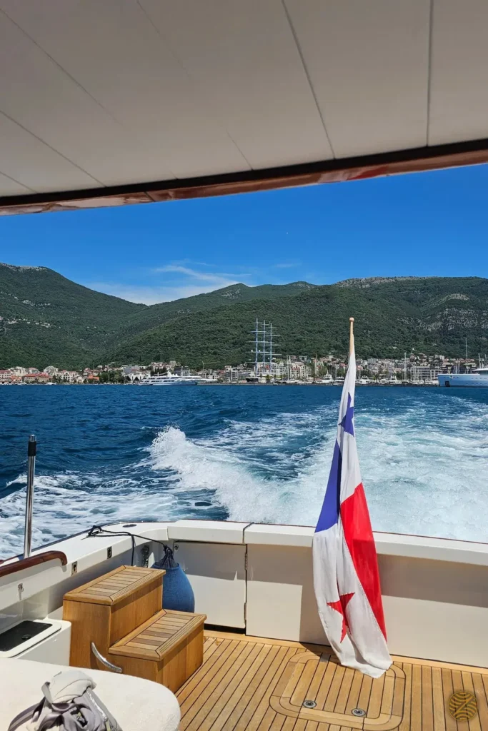 View from the stern of a private yacht leaving Porto Montenegro, with superyachts and the hills of Tivat behind